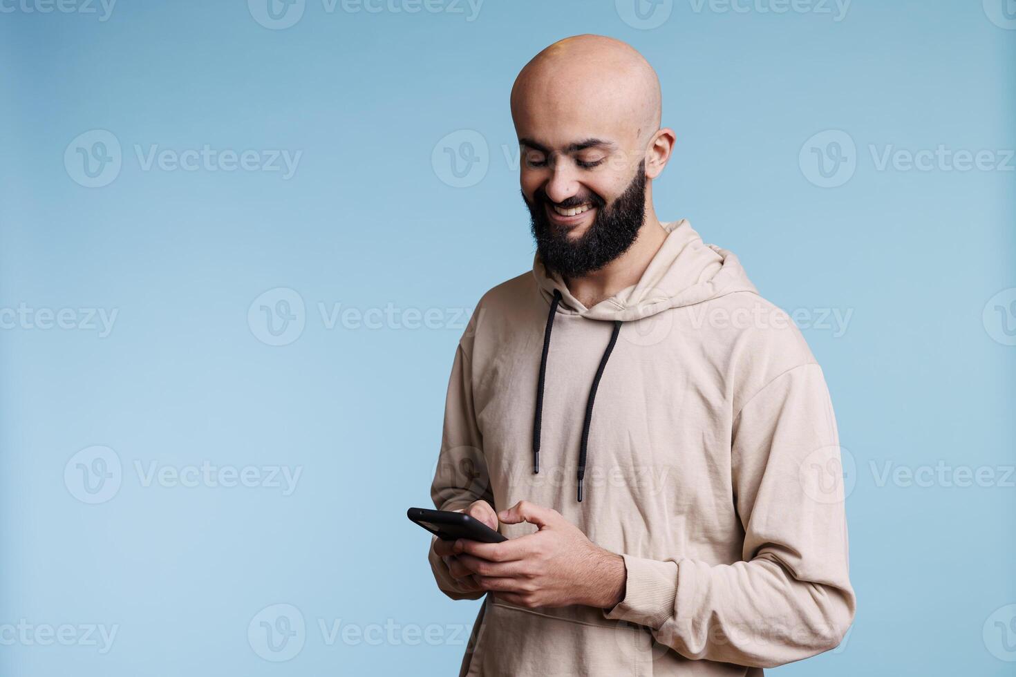 Smiling arab man typing message on smartphone, having fun online communication. Cheerful carefree person texting online while using social media application on mobile phone photo