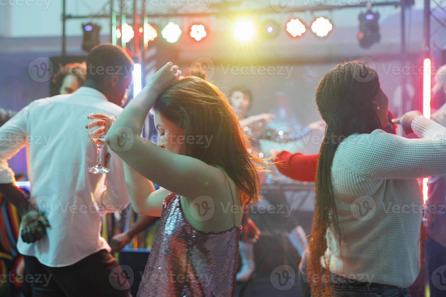 joven mujer participación alcohol bebida vaso y bailando en concurrido Club nocturno. diverso personas ir de fiesta en pista de baile y disfrutando bebidas mientras asistiendo discoteca en club foto