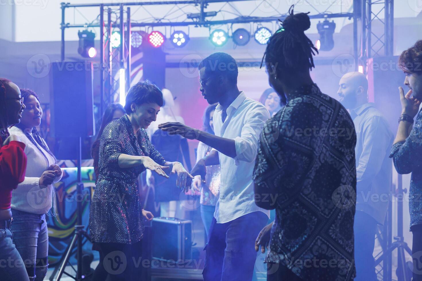 Cheerful dancers doing dance battle while having fun and partying with friends in nightclub. Smiling carefree man and woman showing moves on club dancefloor with spotlights photo