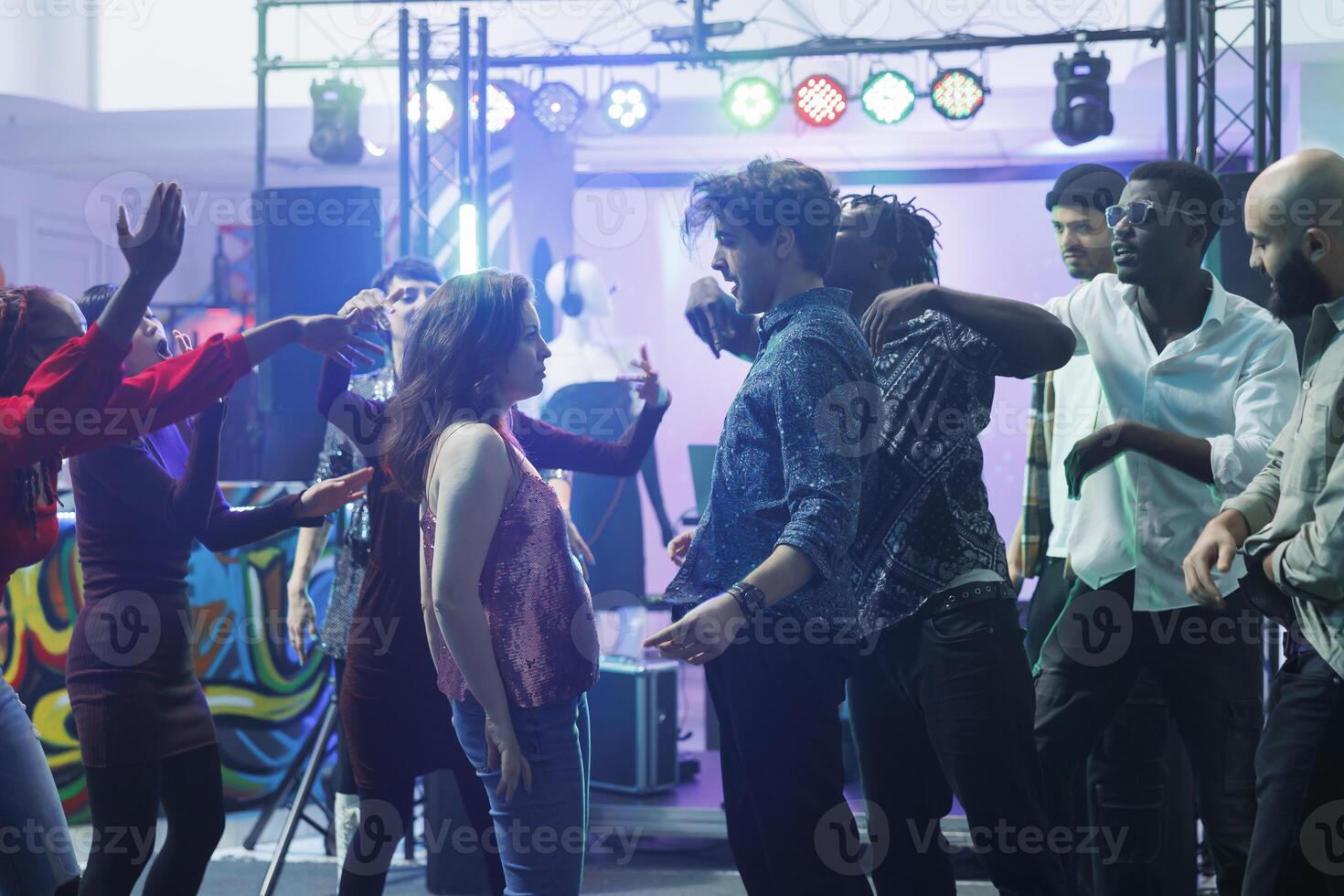 Passionate couple standing on crowded dancefloor ready for dance battle in nightclub. Man and woman showing moves and improvising at discotheque while partying with friends in club photo