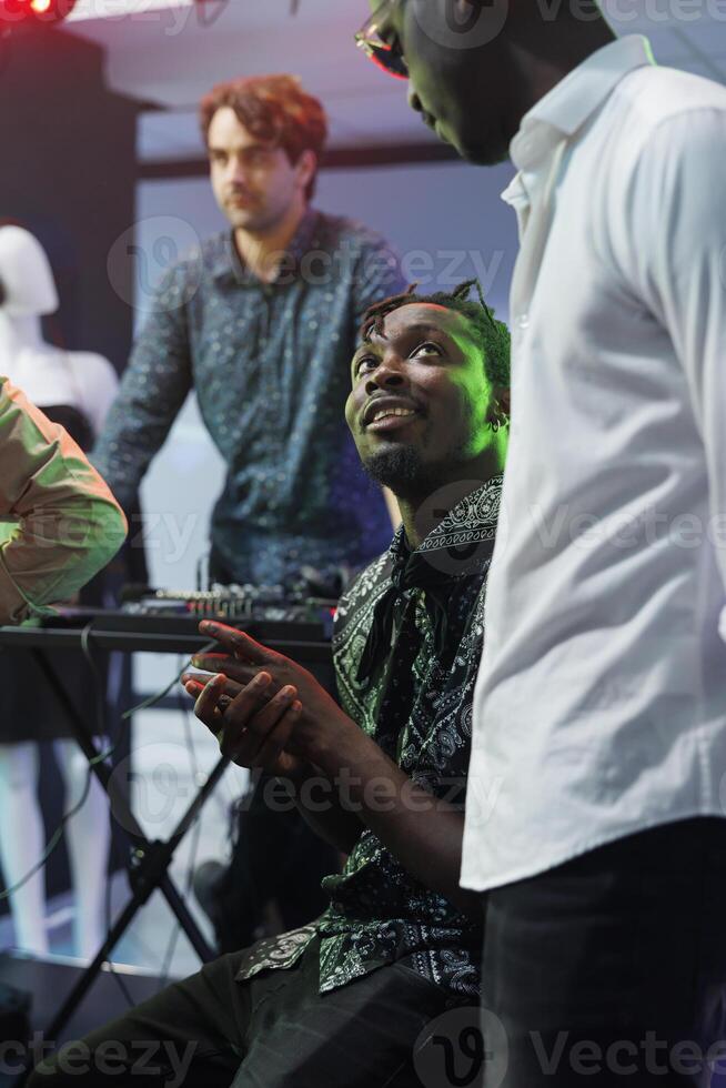 African american friends chatting while clubbing together in nightclub. Young men talking while resting near stage in club, relaxing at party and enjoying nightlife leisure activity photo
