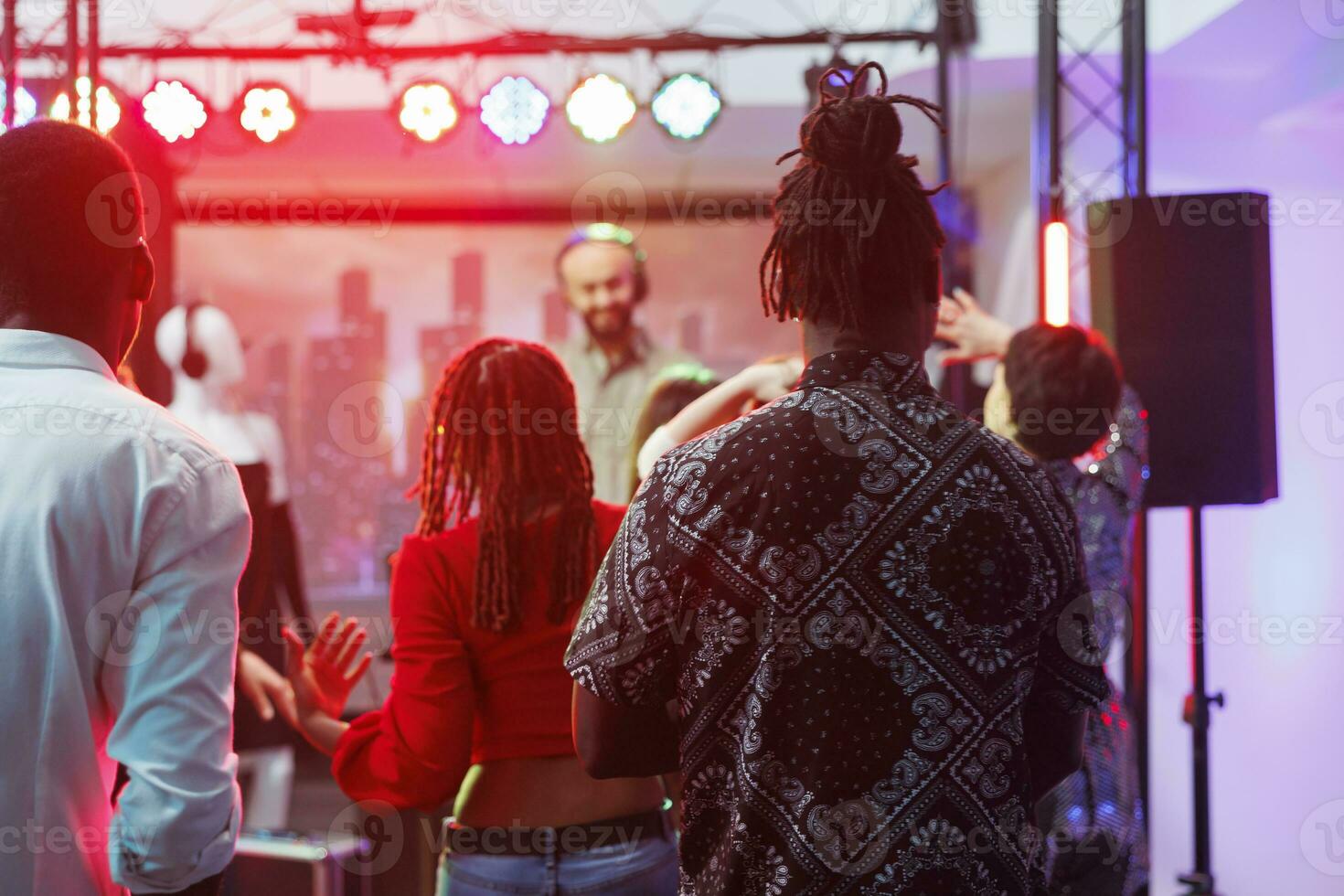 Diverse people clubbing on dancefloor at dj performance party in nightclub. Men and women clubbers crowd attending discotheque, dancing and enjoying nightlife at music festival photo