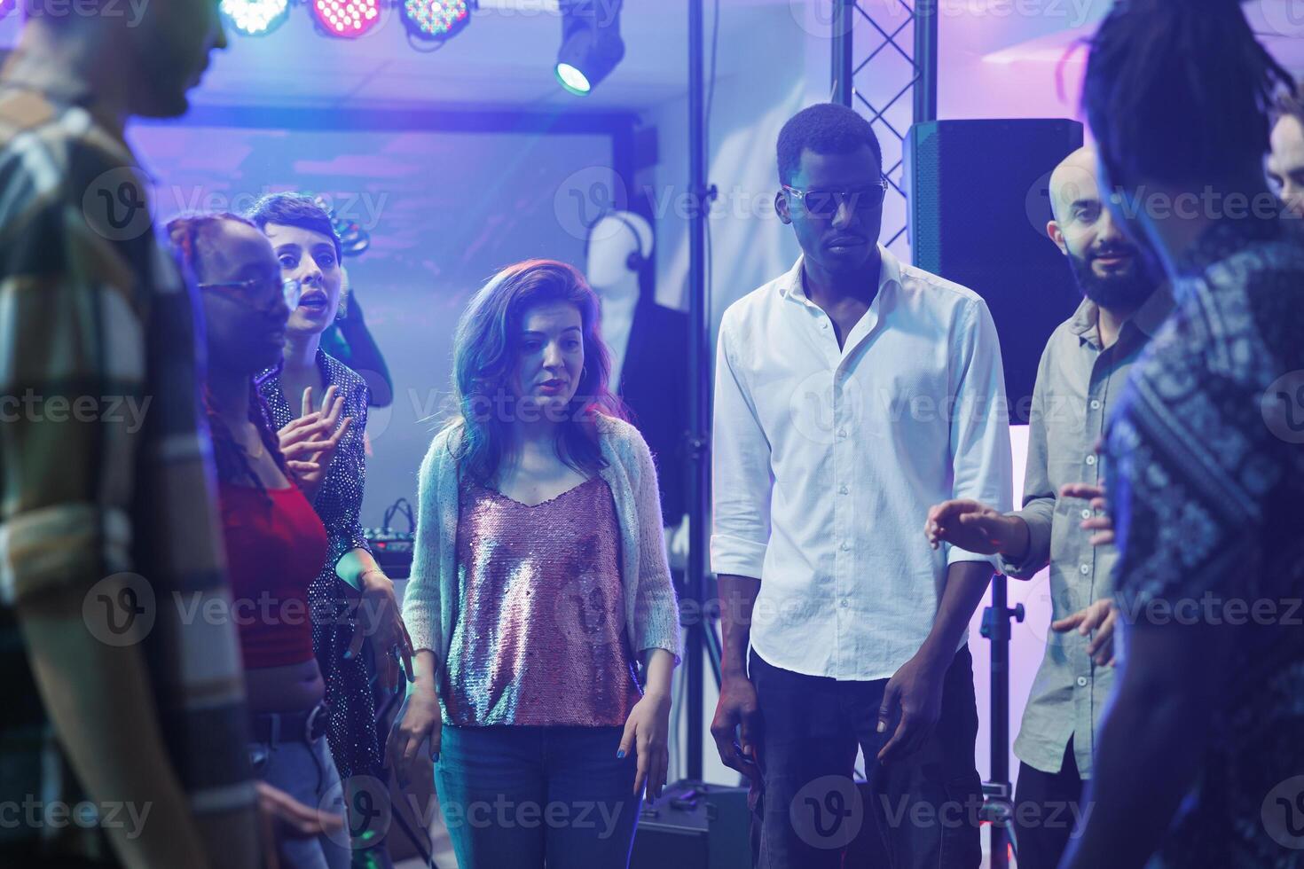 Young friends chatting while partying on dancefloor and improvising dance battle in crowded nightclub. Diverse people having fun and talking while clubbing and celebrating photo