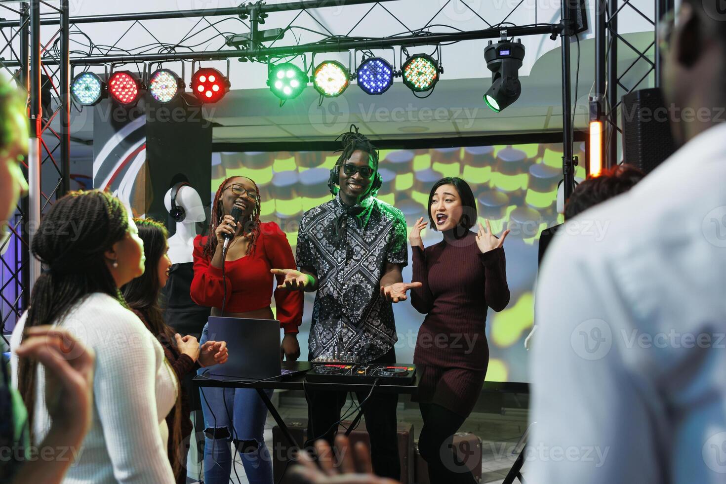 Smiling cheerful women singers and man dj playing on stage at live music concert in nightclub. Carefree energetic musicians band performing at club party social gathering photo