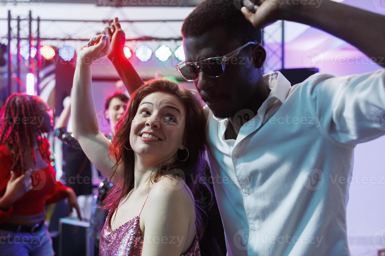 Romantic couple dancing together while relaxing at nightclub party event. Young african american boyfriend and caucasian girlfriend moving on dancefloor, enjoying nightlife photo