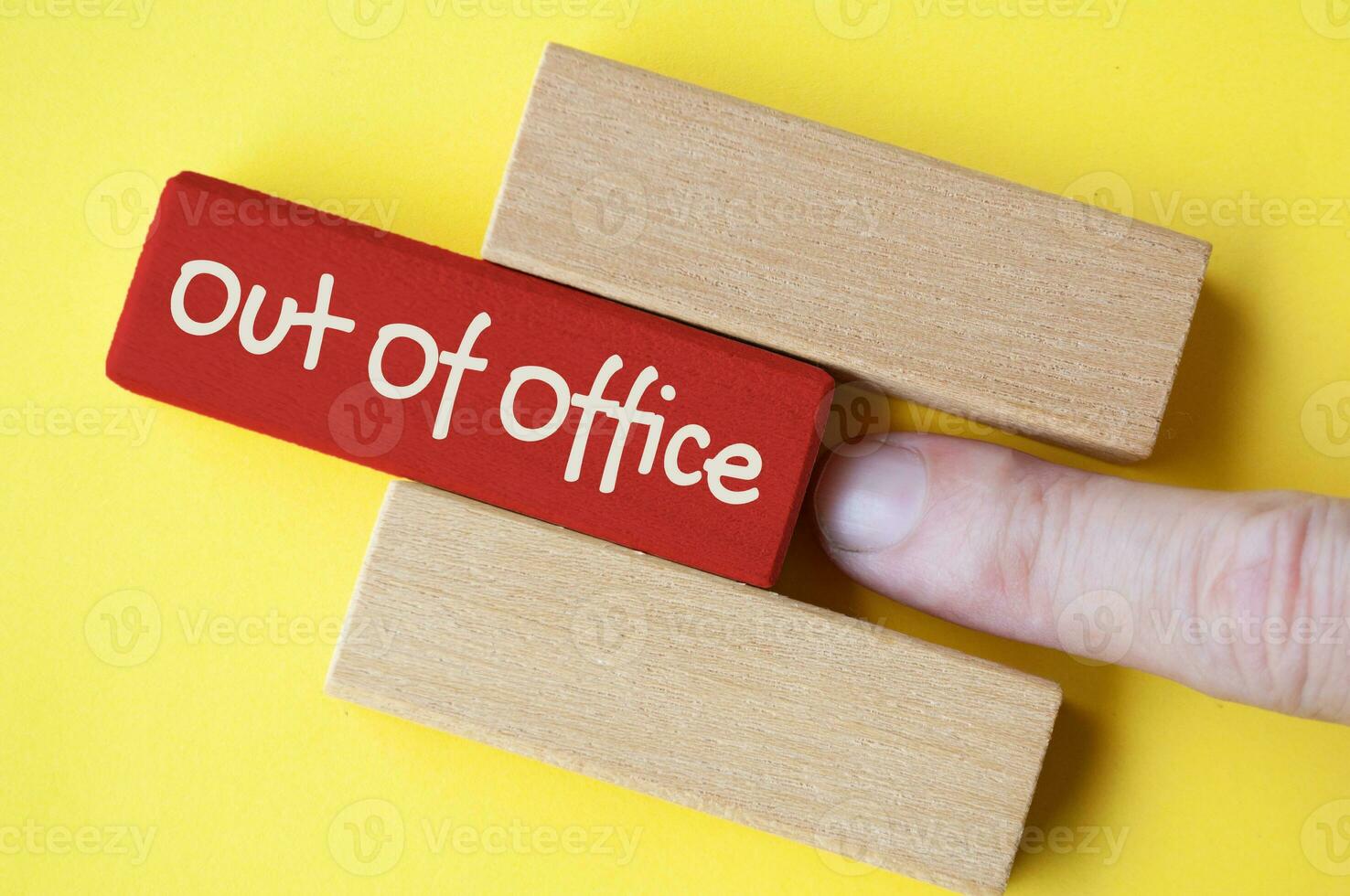 Finger pushing out red wooden block with out of office text on yellow cover background photo