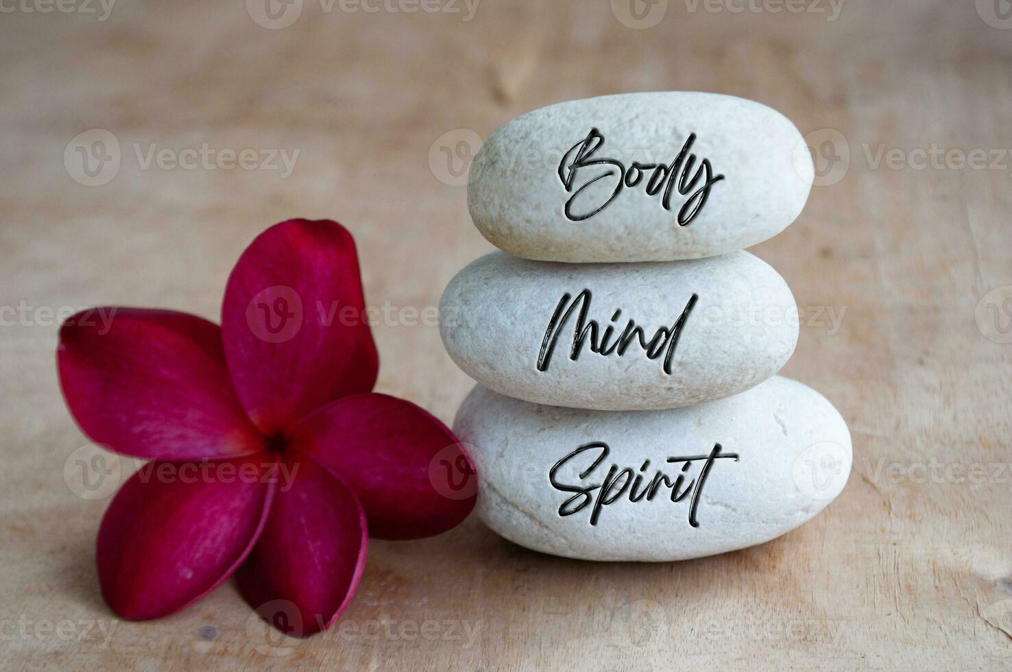 Body, Mind and Soul text engraved on white zen stones with red flower. Meditation and spa concept photo