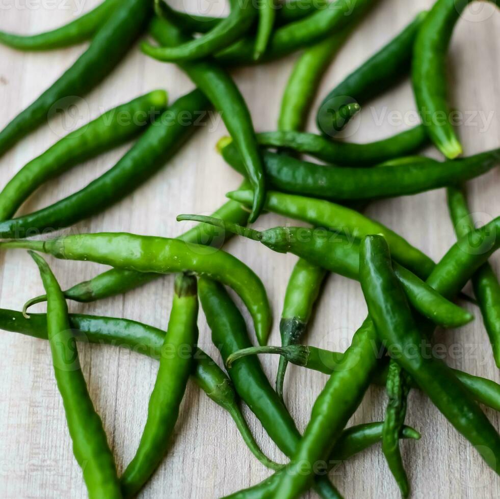 Fresh Green chili pepper on plain wooden table, green essential vegetables for all essential foods, view of unpeeled vegetables with plain background photo