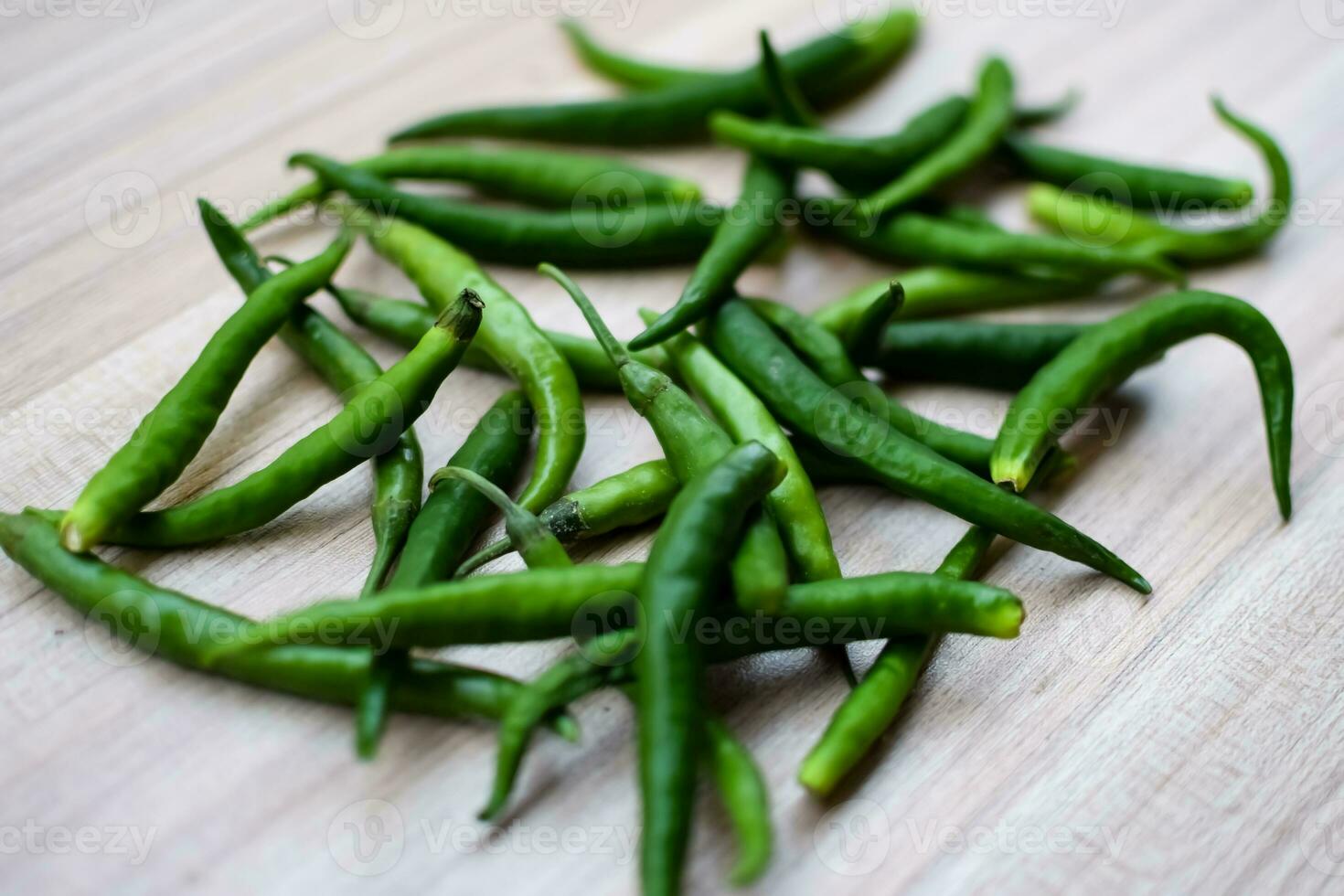 Fresh Green chili pepper on plain wooden table, green essential vegetables for all essential foods, view of unpeeled vegetables with plain background photo