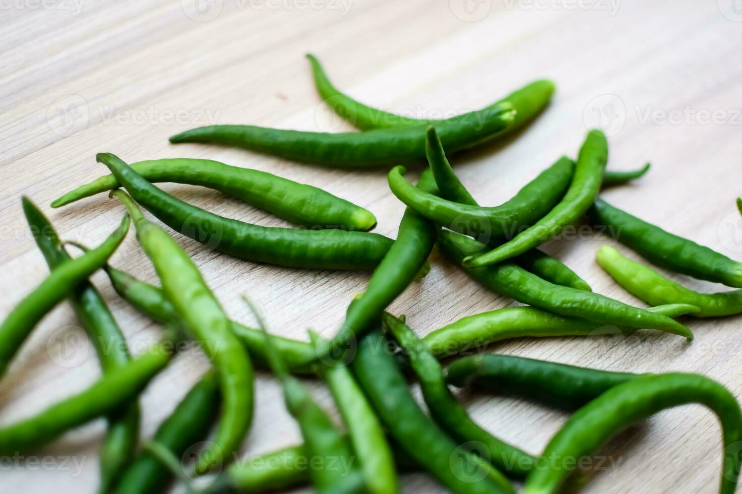 Fresh Green chili pepper on plain wooden table, green essential vegetables for all essential foods, view of unpeeled vegetables with plain background photo