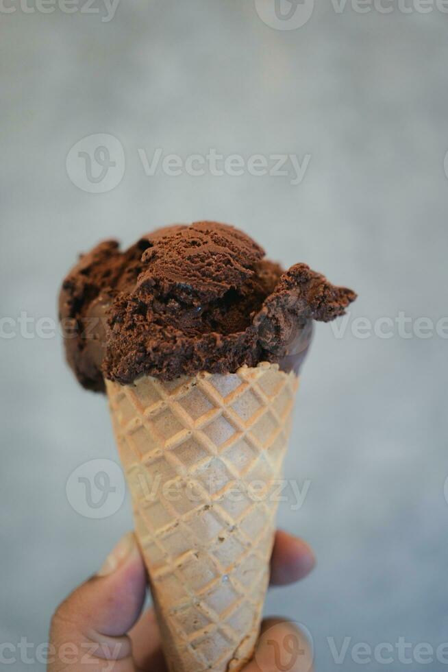 A hand holding of chocolate ice cream in a waffle cone photo