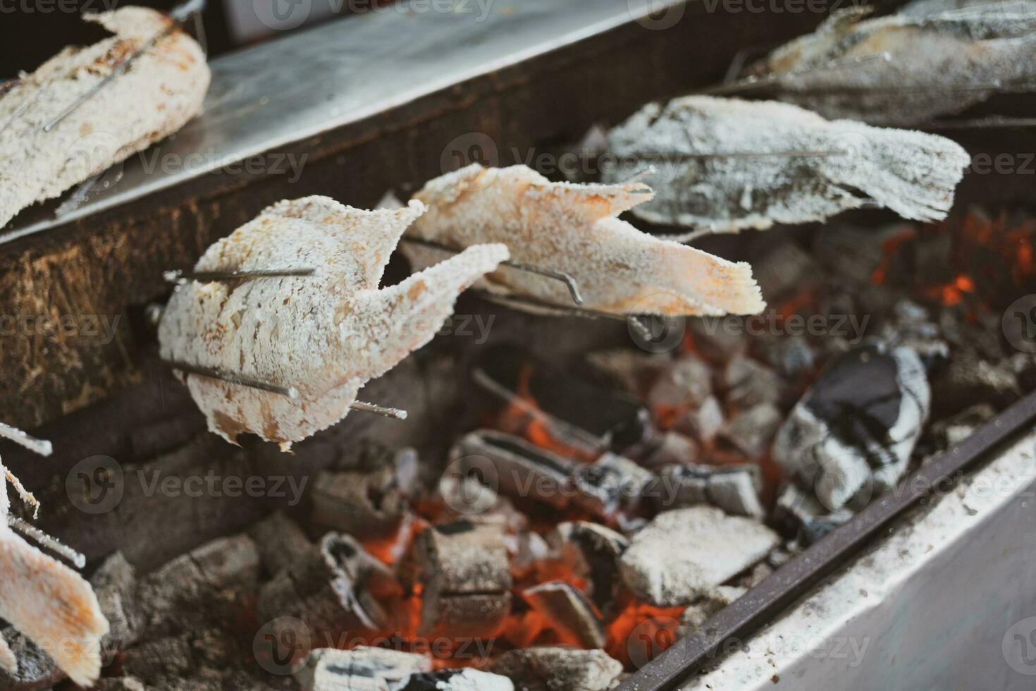 Fish coated with salt grill on the fire. Grilled fish on the fireplace with an automatic rotate machine. photo