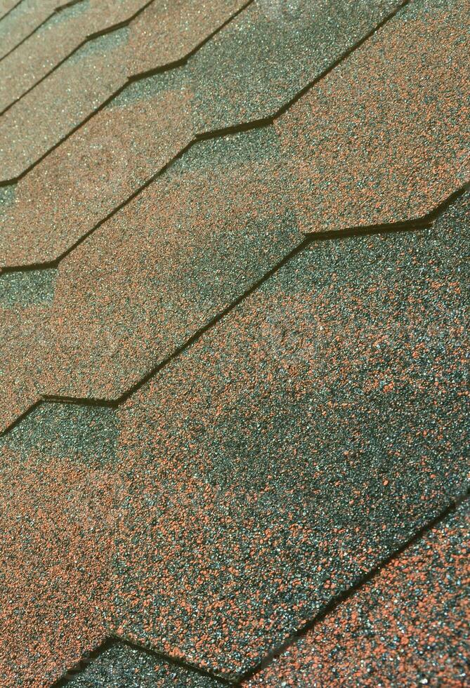 The texture of the roof with bituminous coating. Rough bituminous mosaic of red and brown flowers. Waterproof roofing photo