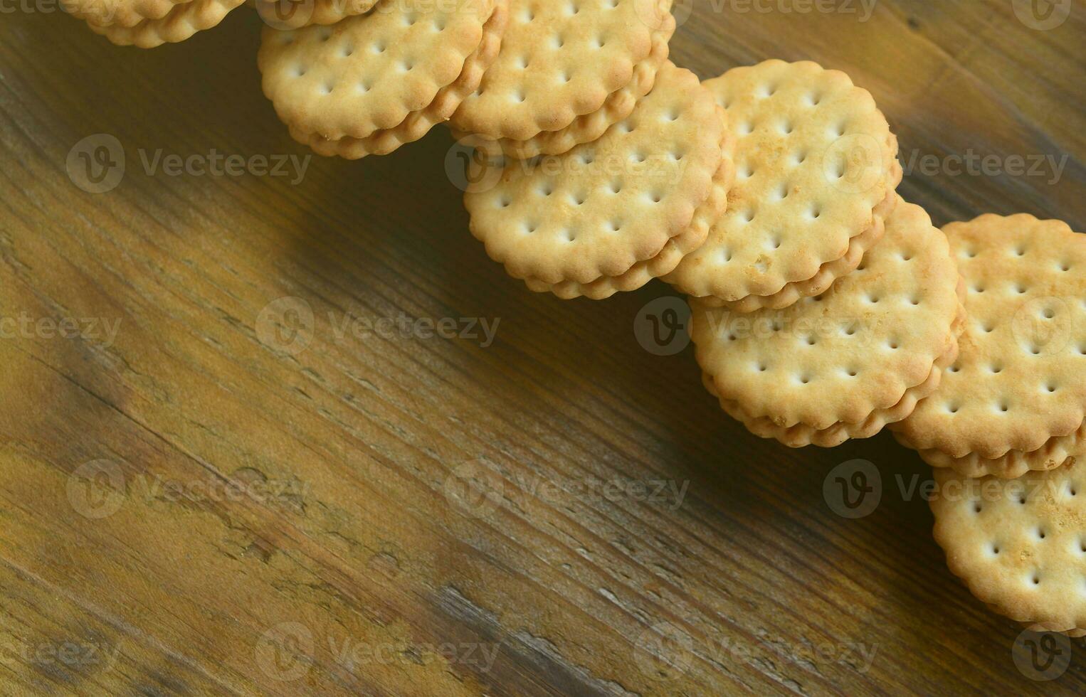 A round sandwich cookie with coconut filling lies in large quantities on a brown wooden surface. Photo of edible treats on a wooden background with copy space