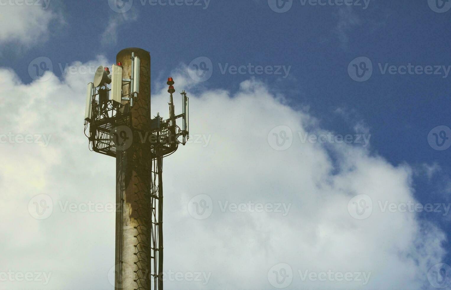 High metal chimney of industrial plant with ladder in the form of metal braces against the background of a cloudy blue sky photo