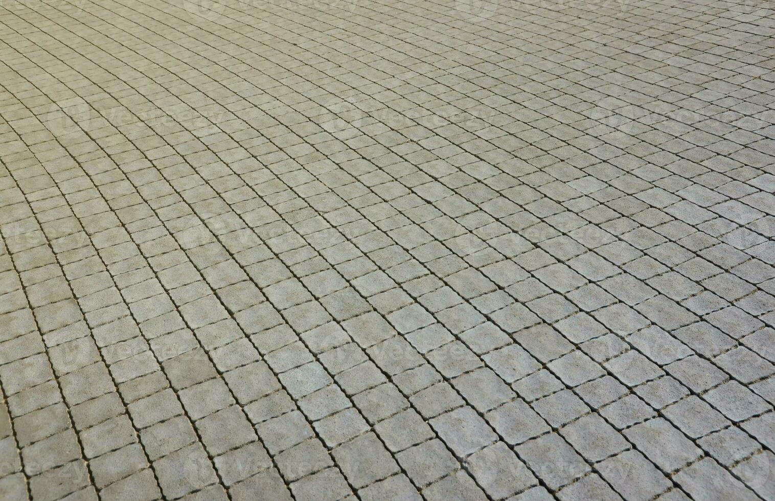 Gray color paving slabs in the pedestrian street sidewalk. Rough cobblestone pattern with many square shaped stones photo