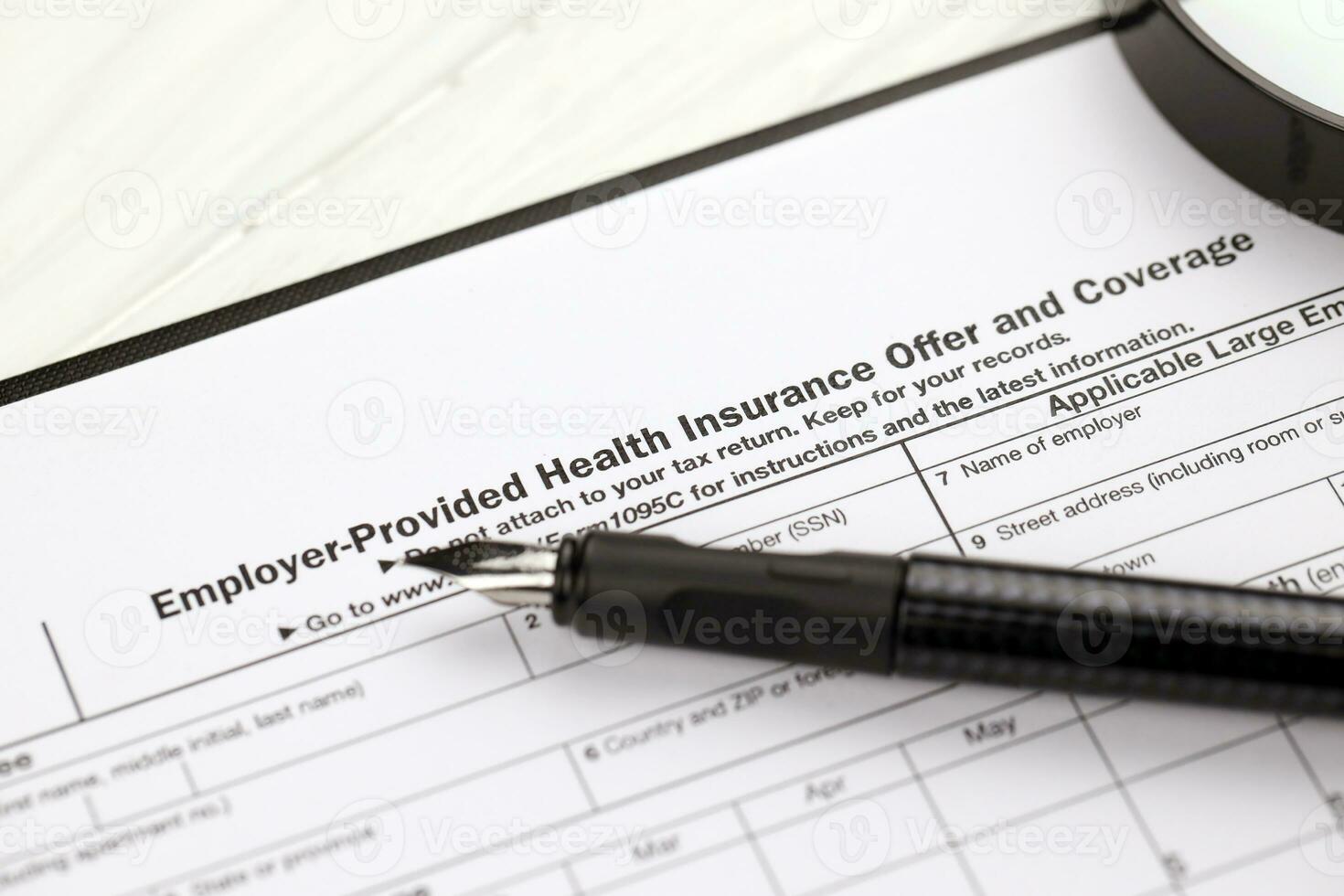 IRS Form 1095-C Employer-Provided Health Insurance Offer and Coverage tax blank on A4 tablet lies on office table with pen and magnifying glass photo