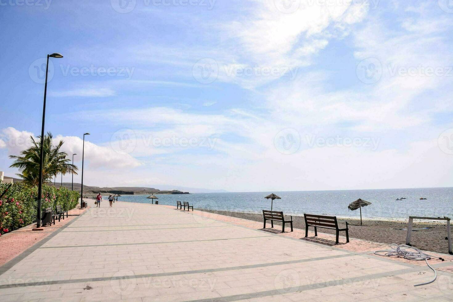a walkway along the beach with benches and umbrellas photo
