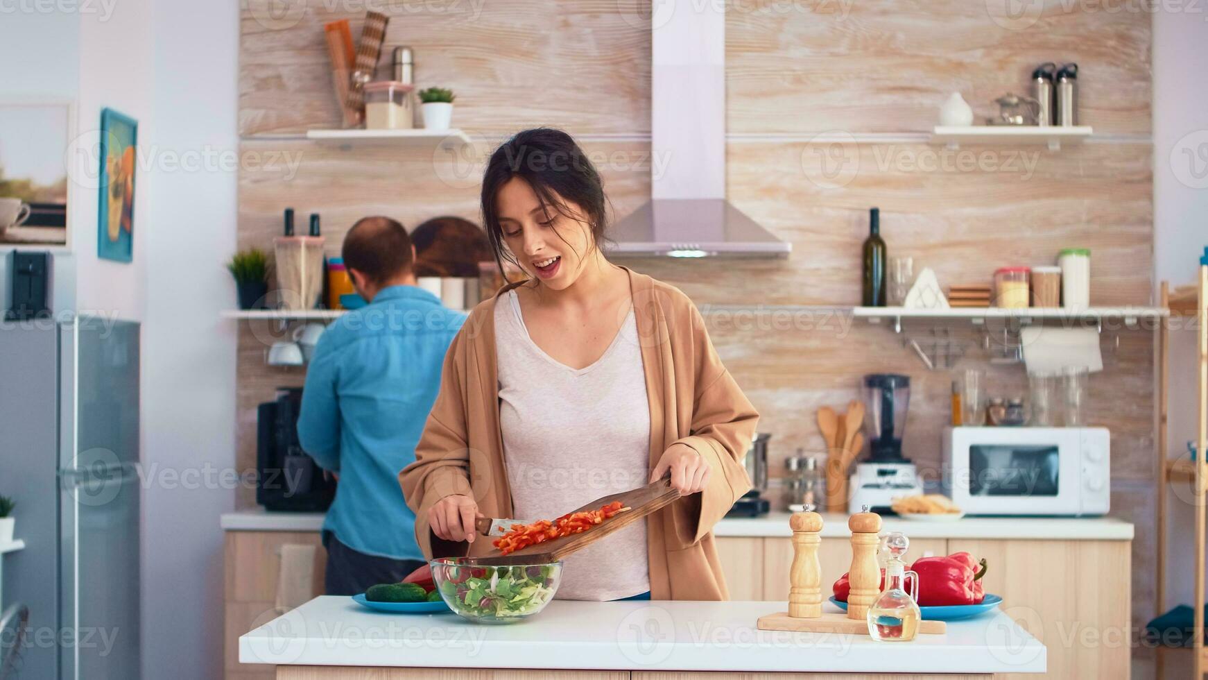 Husband kissing wife cheek while she is chopping bell pepper on cutting board in kitchen. Cooking preparing healthy organic food happy together lifestyle. Cheerful meal in family with vegetables photo