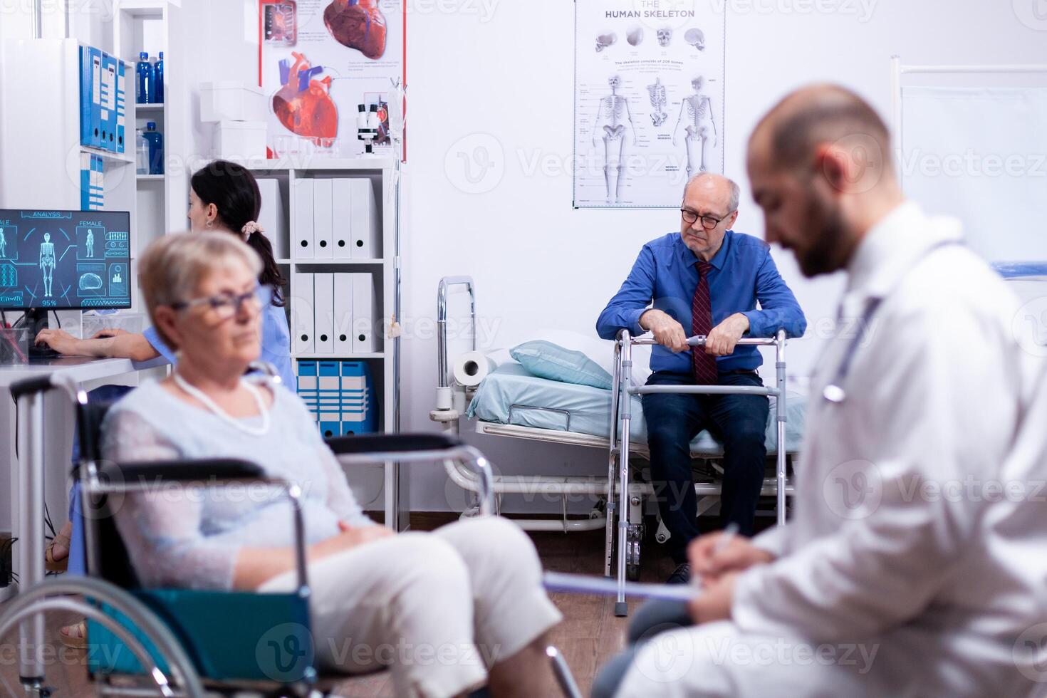 Invalid senior man with walking frame in busy modern private recovery clinic. Man with disabilities ,walking frame sitting in hospital bed. Health care system, patients. photo