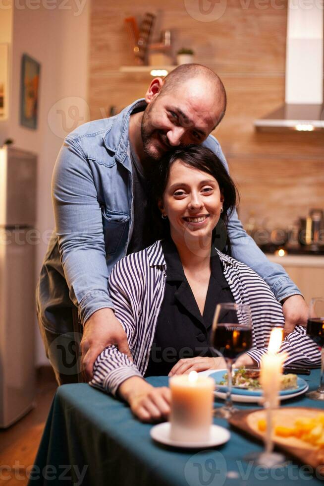 Romantic couple looking at webcam during romantic dining. Married people special tender moments, enjoying the meal at candle lights celebration. photo