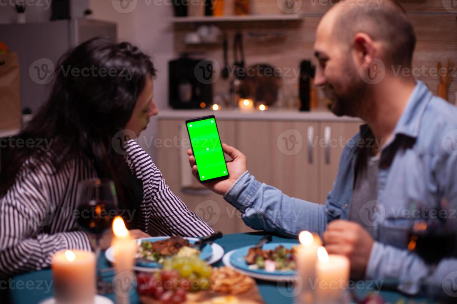 Couple looking at phone with green mock up having romantic dinner. Happy holding phone green screen template chroma key isolated smartphone display using technology internet. photo