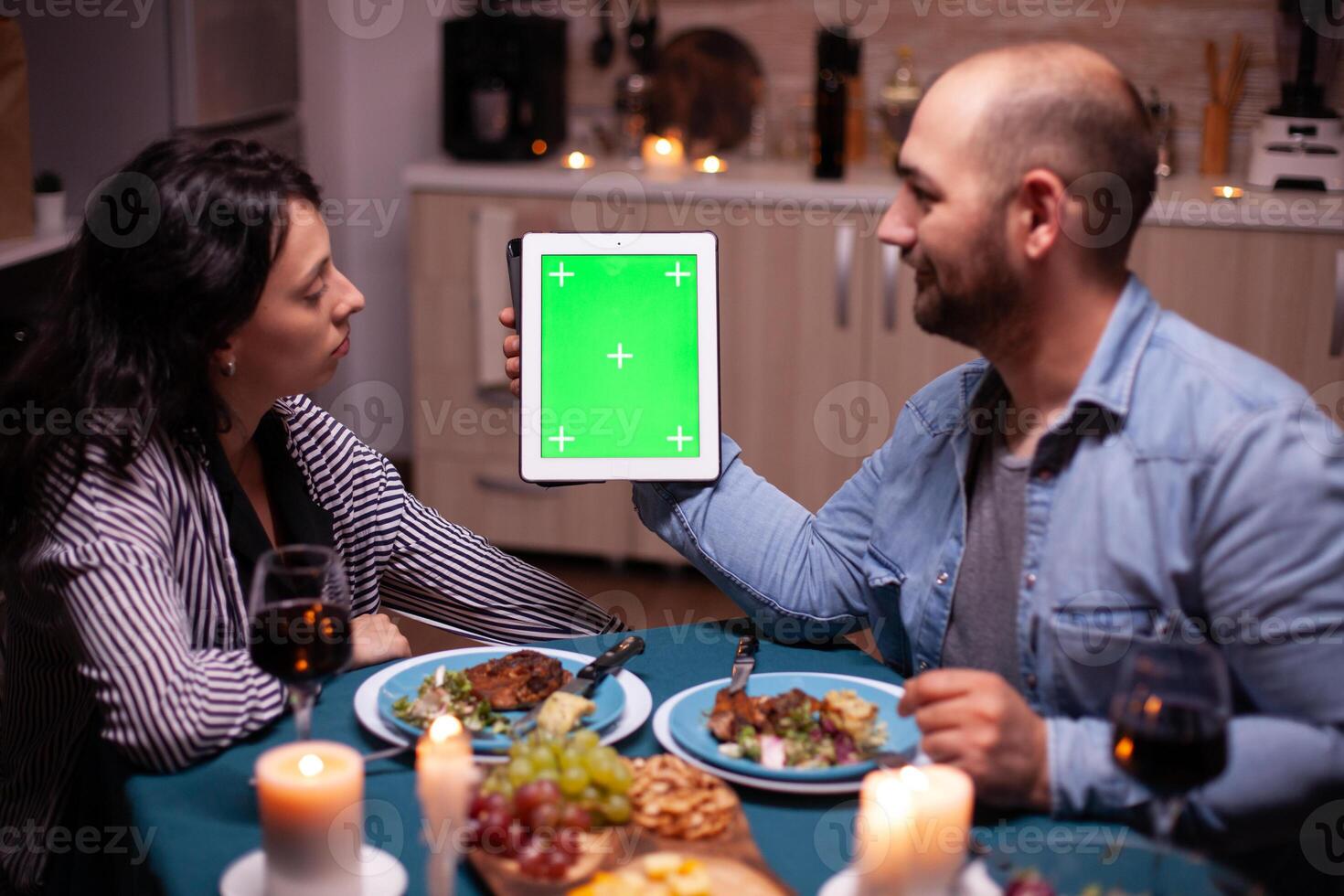 Husband holding tablet with green screen and looking at wife during romantic dinner. photo