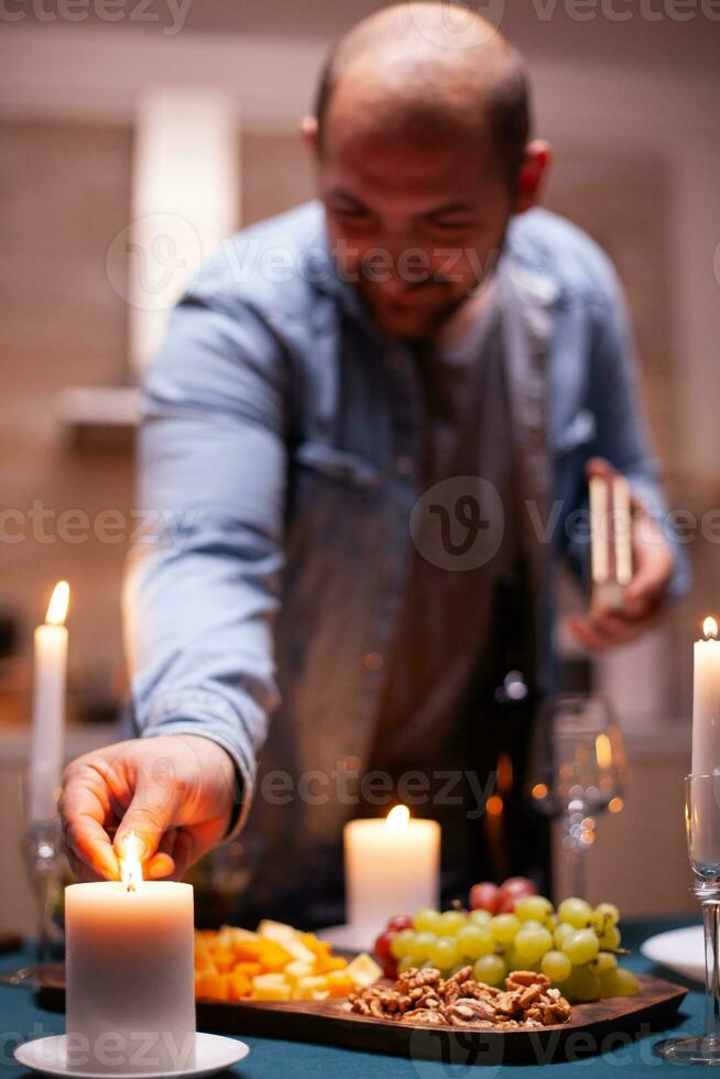 Encendiendo vela con partidos. marido preparando festivo comida con sano comida para aniversario celebracion, romántico fecha, sentado cerca el mesa en cocina. foto