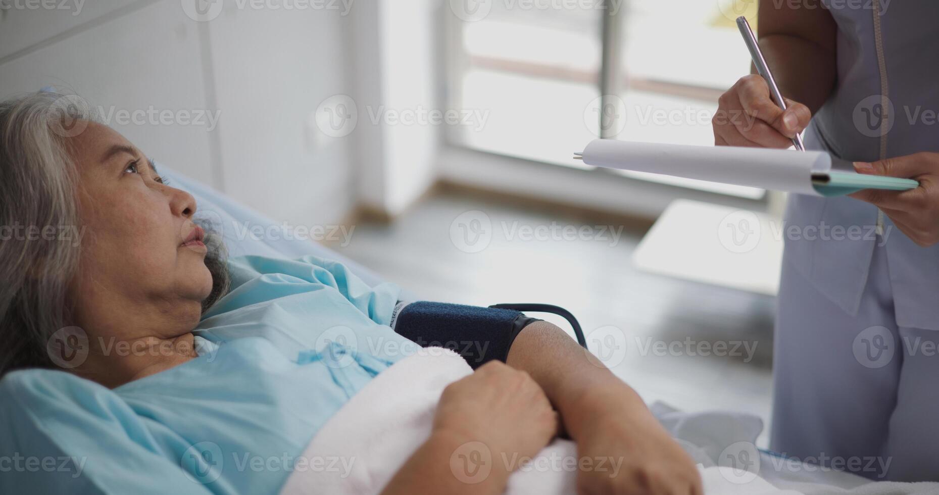 Portrait of Elderly female patient who was admitted lay on a hospital bed while a young nurse explained her illness. photo