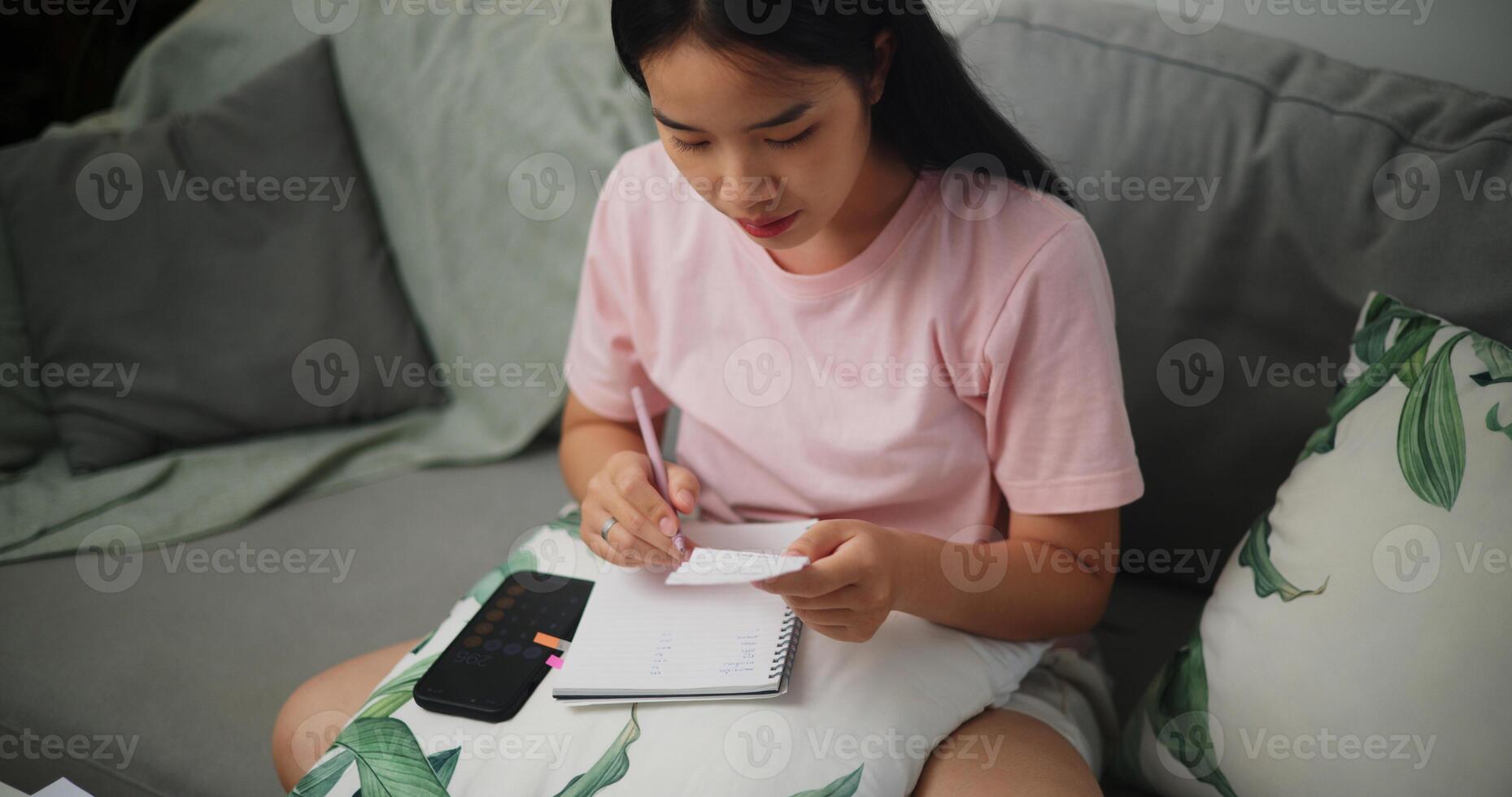 Portrait of Young Asian woman holding paper various expense bills and plans for personal finances and using calculator on smartphone calculate Income and expenses at home,Home finance photo