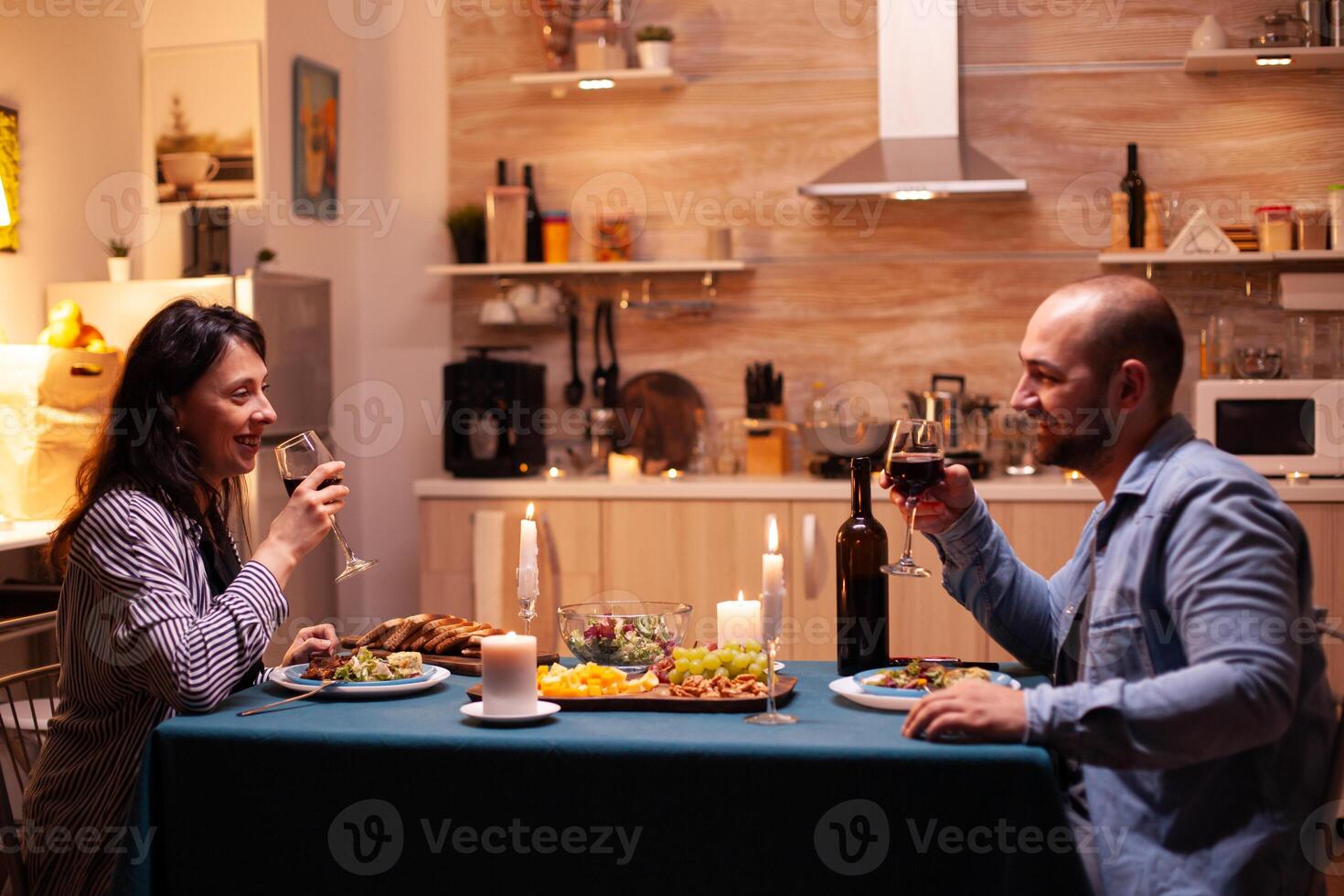 joven Pareja teniendo romántico hora durante cena. contento Pareja hablando, sentado a mesa en comida habitación, disfrutando el comida, celebrando su aniversario a hogar teniendo romántico tiempo. foto