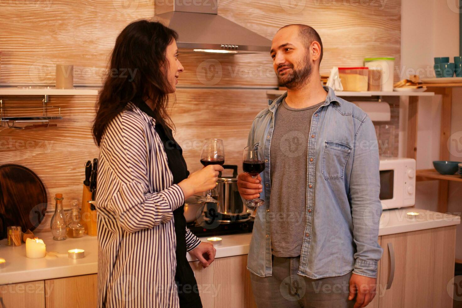 Man and woman having fun during date drinking wine. Adult couple having romantic date at home, in the kitchen, talking, smiling, enjoying the meal in dining room. photo