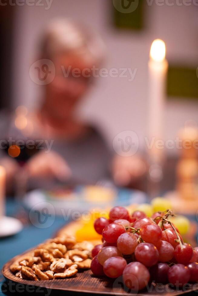 Nuts and grapes sitting on wooden plate during elderly couple festive dinner. Senior couple sitting at the table in kitchen, talking, enjoying the meal, celebrating their anniversary in the dining room. photo