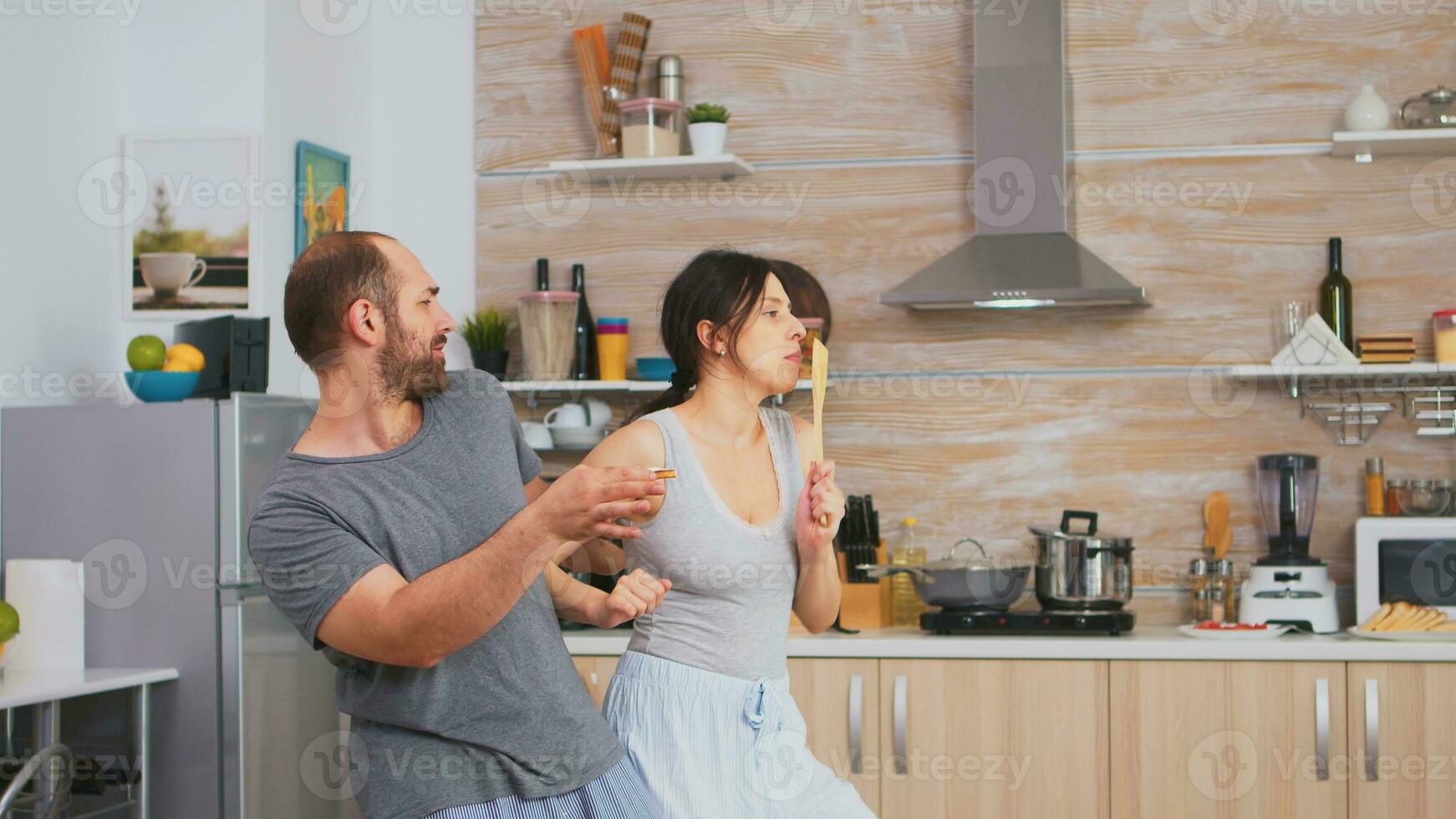 auténtico Pareja bailando en pijama participación batería de cocina durante desayuno. despreocupado esposa y marido riendo teniendo divertido gracioso disfrutando vida auténtico casado personas positivo contento relación foto