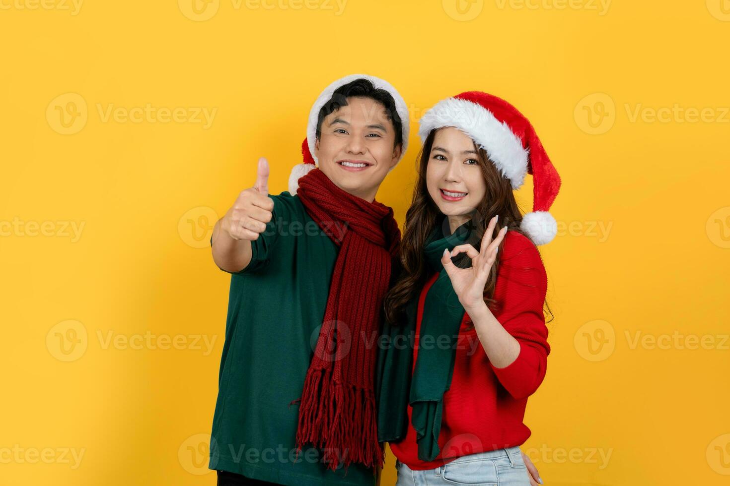 Man and woman wearing sweaters and Santa hats on a bright yellow background. Christmas and Happy New Year holiday concept. photo