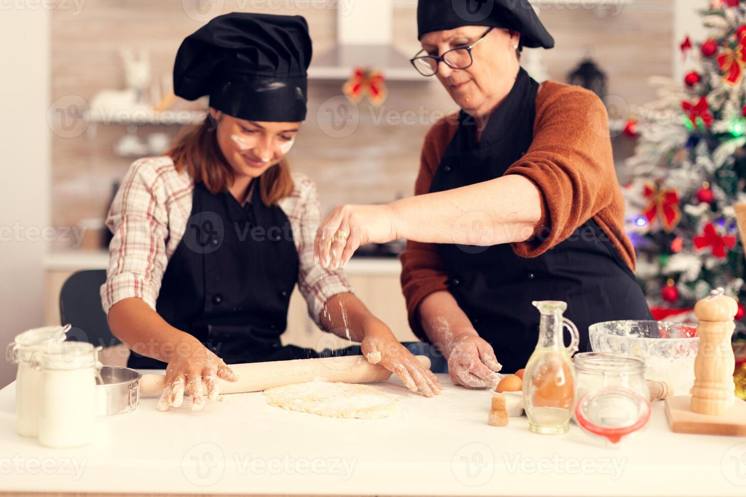 Granddaughter in apron preparing cake on christmas day with grandmother. Happy cheerful joyfull teenage girl helping senior woman preparing sweet cookies to celebrate winter holidays. photo