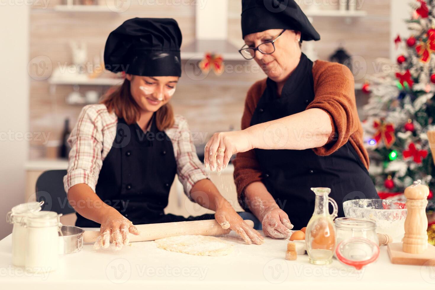 Close up of grandmother on christmas day spreading flour and making dessert with child. Happy cheerful joyfull teenage girl helping senior woman preparing sweet cookies to celebrate winter holidays. photo