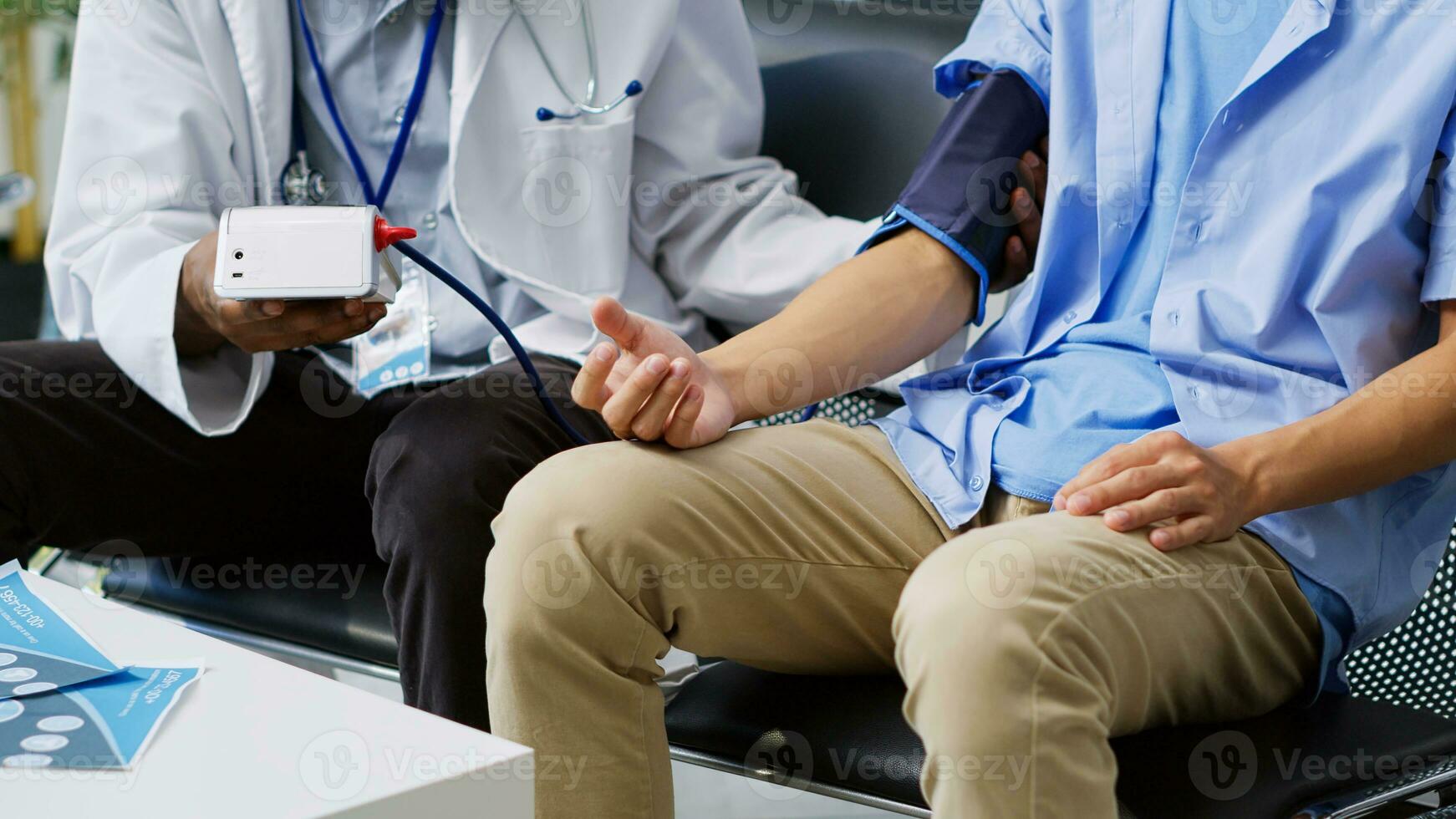 Physician using medical tonometer to measure patient pulse pressure and hypertension in hospital waiting area. African american medic doing cardiology exam with asian man during checkup visit photo