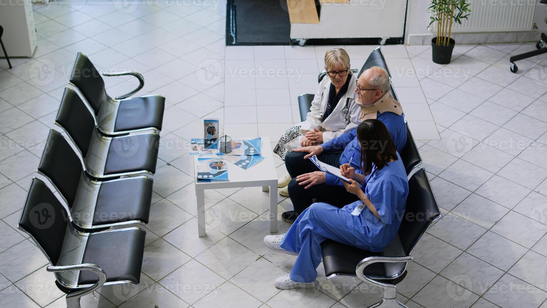 Senior physician medic and assistant helping elderly patient to take off cervical neck collar during checkup visit consultation in hospital waiting area. Old man receiving medicine support photo