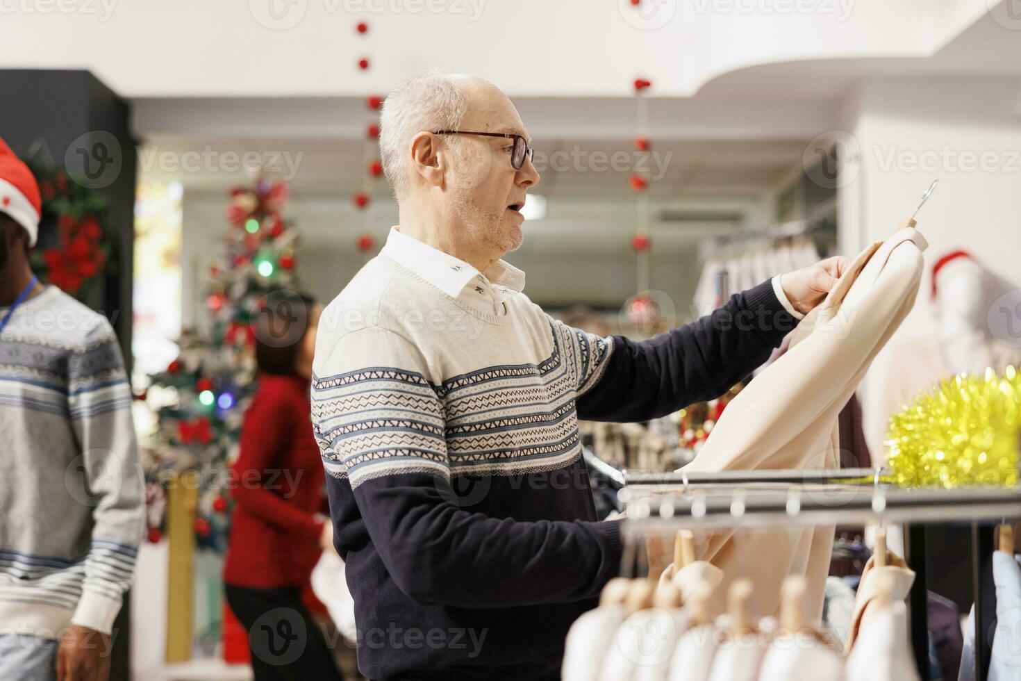Senior person looks at clothes fabric in clothing store with festive ornaments, looking for christmas gifts and seasonal dinner outfit. Shopper searching for items on promotional sales. photo