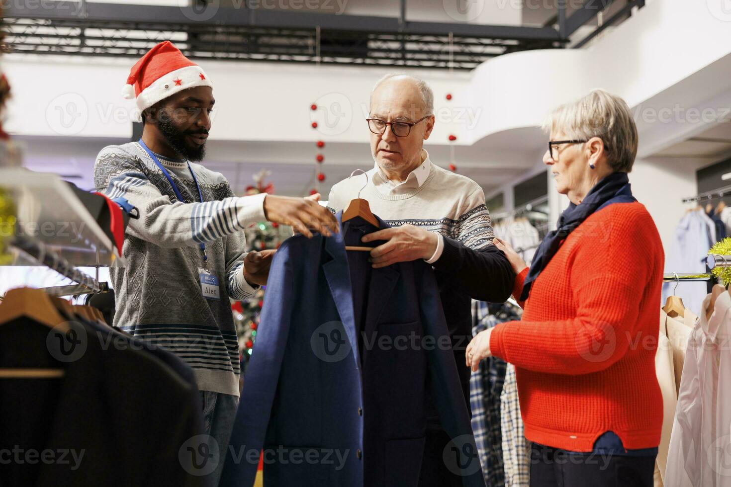 Man employee helping clients to choose jackets and blazers, making preparations for upcoming christmas event. Senior couple shopping for clothes in retail store, buying merchandise on sale. photo