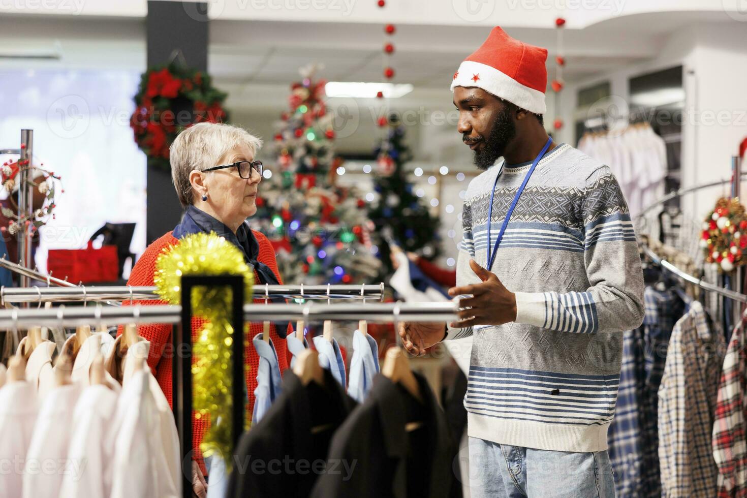 Worker helping elderly woman to choose right fit of formal attire, preparing to attend festive dinner on christmas holiday. African american store employee recommending clothes for client. photo