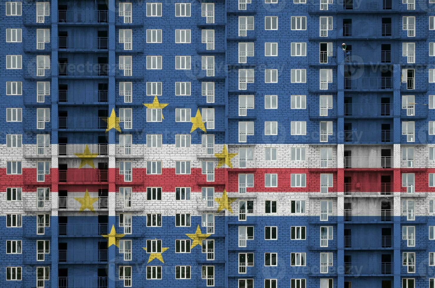 Cabo verde flag depicted in paint colors on multi-storey residental building under construction. Textured banner on brick wall background photo