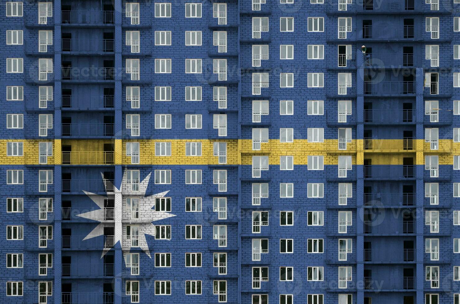 Nauru flag depicted in paint colors on multi-storey residental building under construction. Textured banner on brick wall background photo