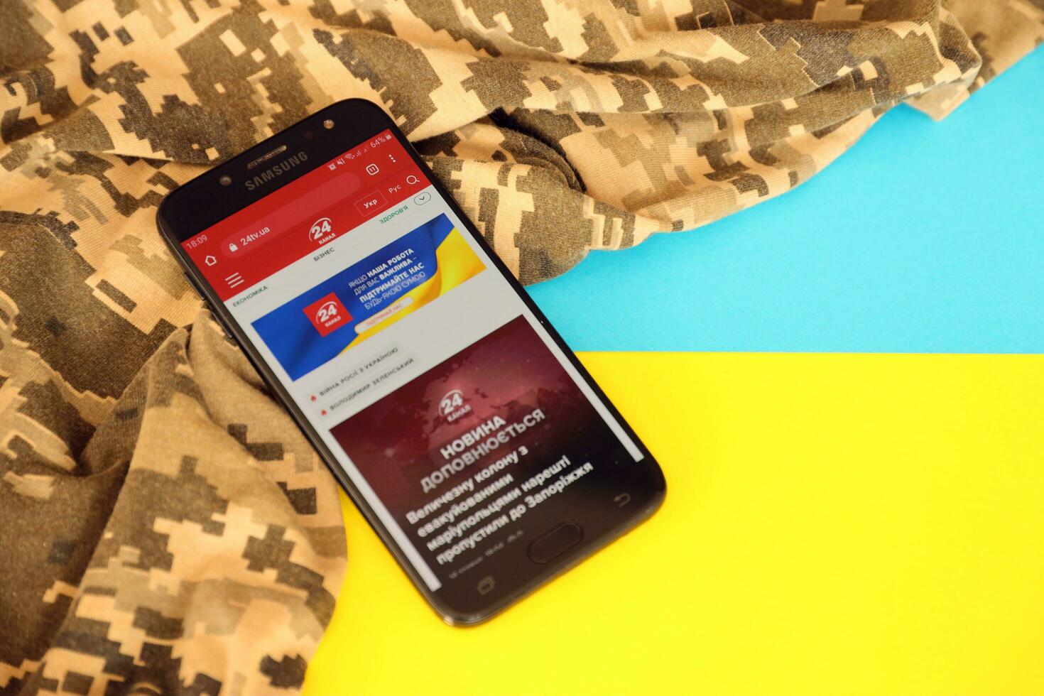 KYIV, UKRAINE - 4 MAY, 2023 24tv ukrainian news portal on smartphone screen with ukrainian flag and camouflage fabric photo