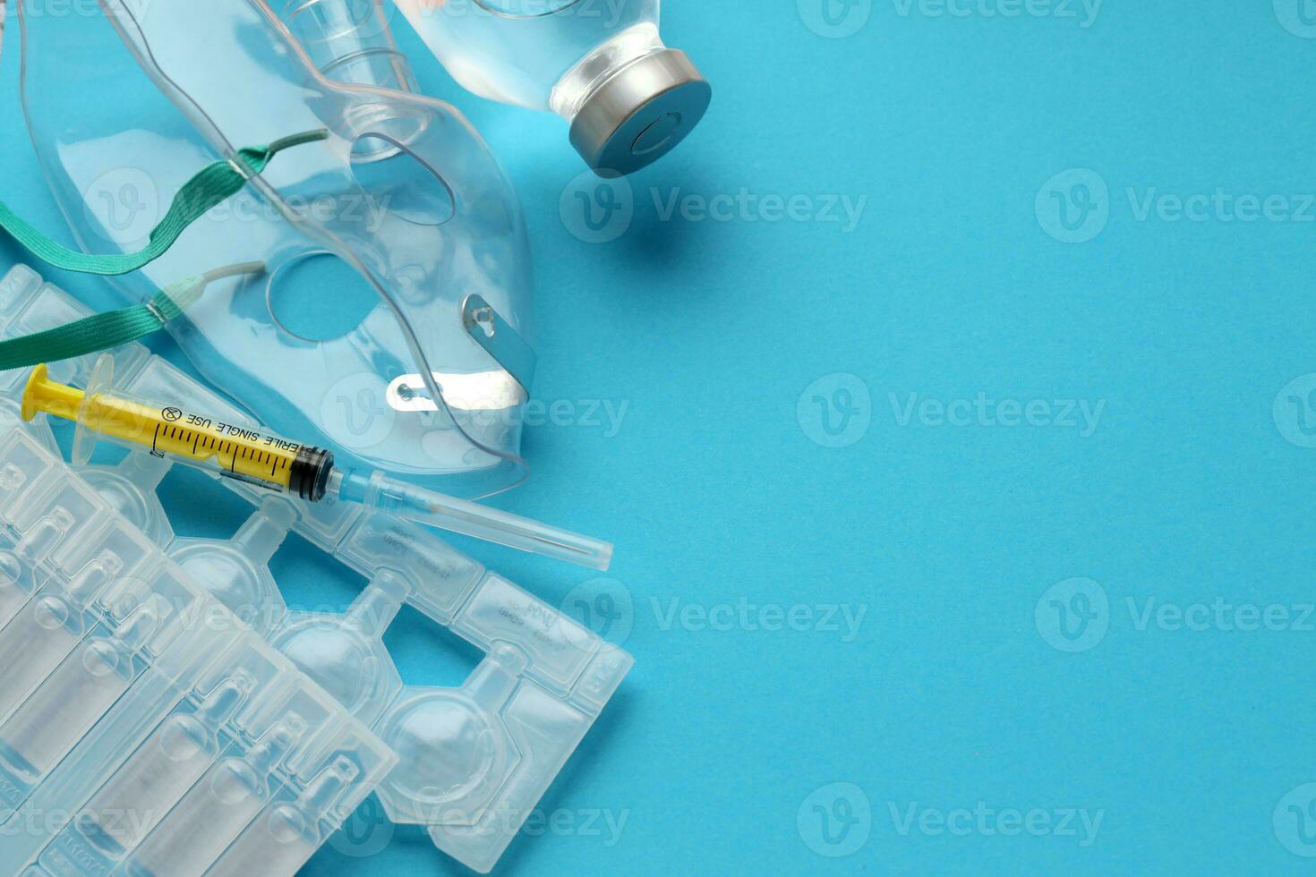 Coronavirus treatment concept. A medical face mask nebulizer for treatment of respiratory tract and packs of ampoules flat layed on blue background photo