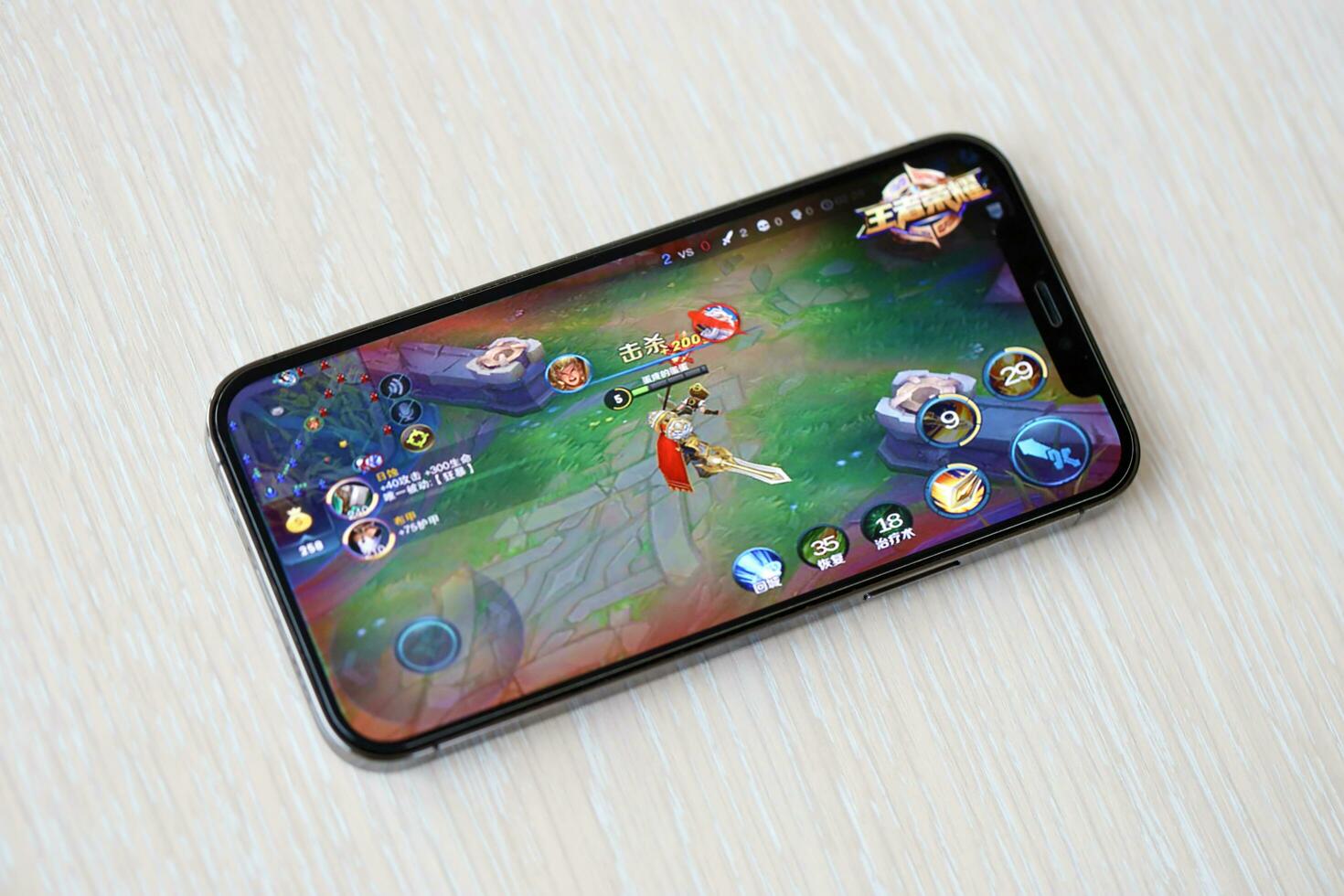 Honor of Kings mobile iOS game on iPhone 15 smartphone screen on wooden table during mobile gameplay photo