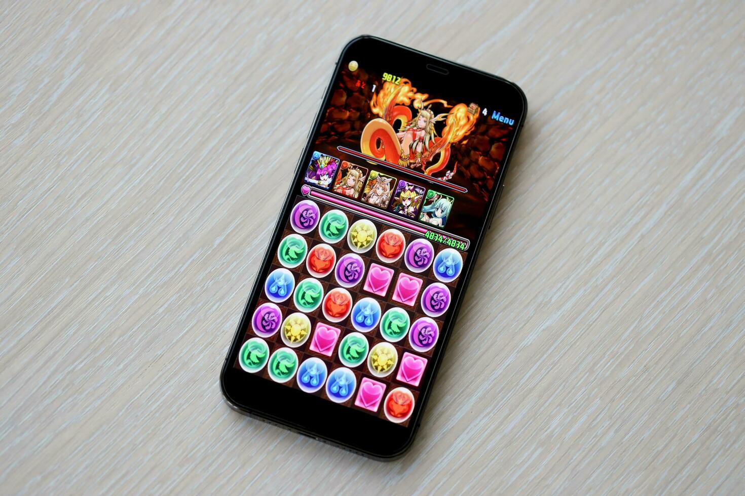 Puzzle and dragons mobile iOS game on iPhone 15 smartphone screen on wooden table during mobile gameplay photo