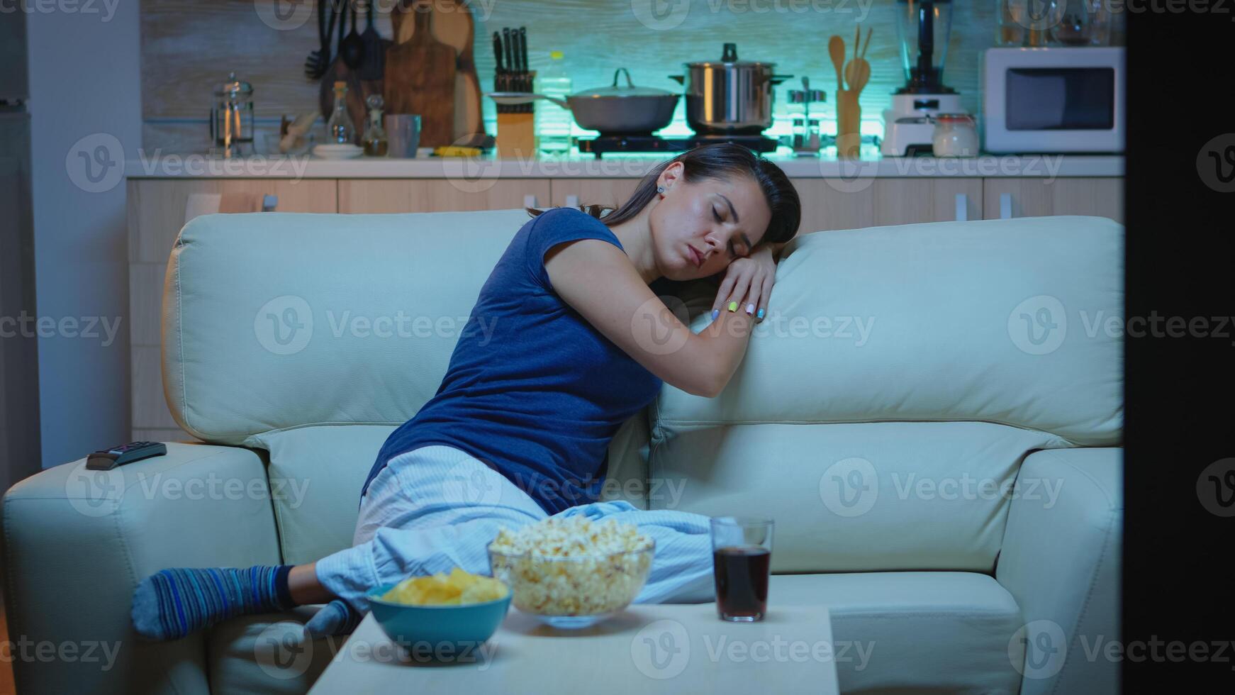 Woman sleeping on a sofa in front of TV while watching a bored movie. Tired exhausted lonely sleepy lady in pajamas falling asleep sitting on cozy couch in living room, closing eyes at night photo