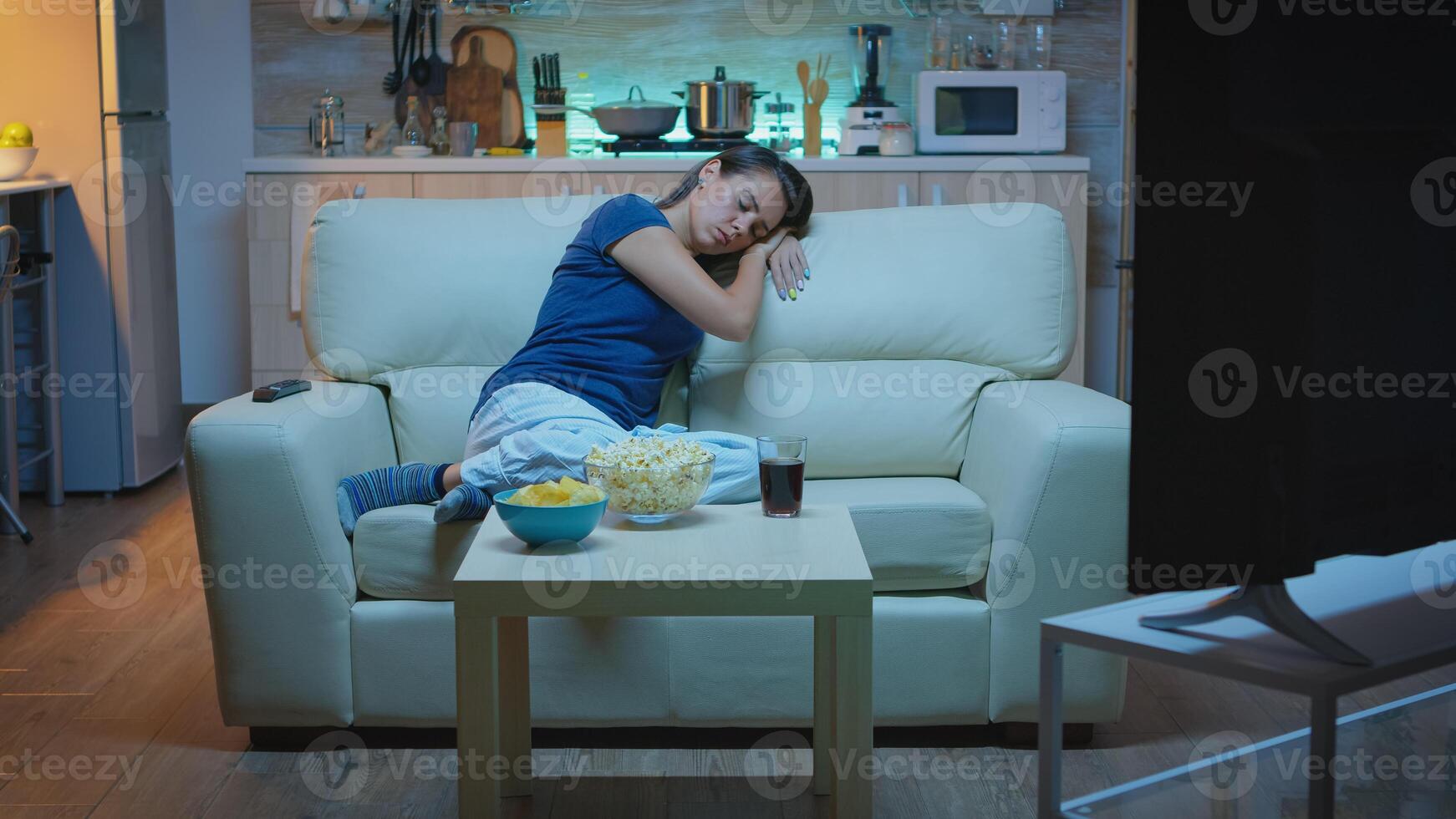 Housewife falling asleep in living room on sofa in front of tv. Tired exhausted lonely sleepy lady in pajamas sleeping on comfortable couch in living room, closing eyes while watching tv at night photo